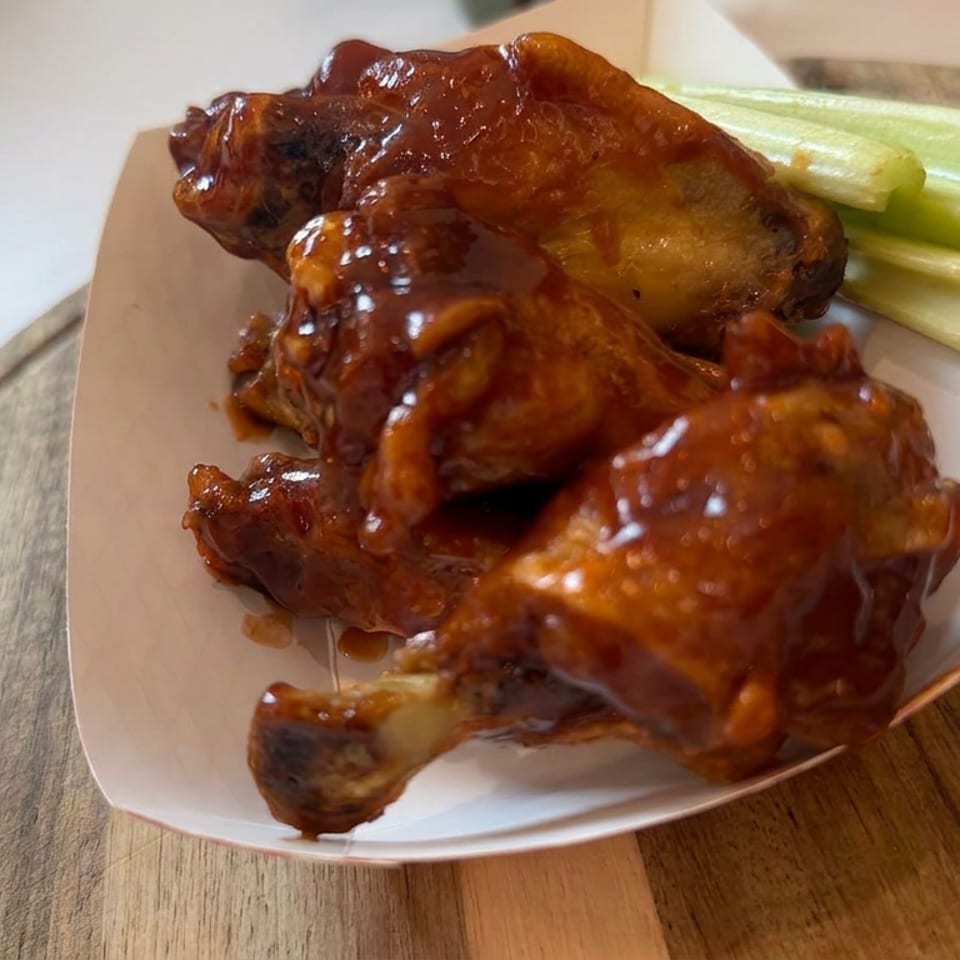 Glazed chicken wings and drumettes served with celery sticks on a white plate atop a wooden table.